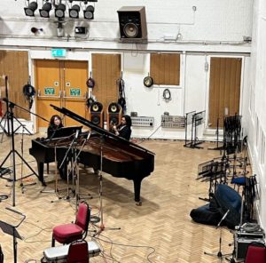 author Nancy Manet records at song at a grand piano that is at the Abbey Road studios in london. many wires, microphones and equipments are everywhere #alaac2023