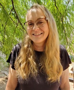 Michelle Buvala, illustrator of children's books, stand outside under a mesquite tree. she is smiling and looking into the camera. kidlit illustrator author